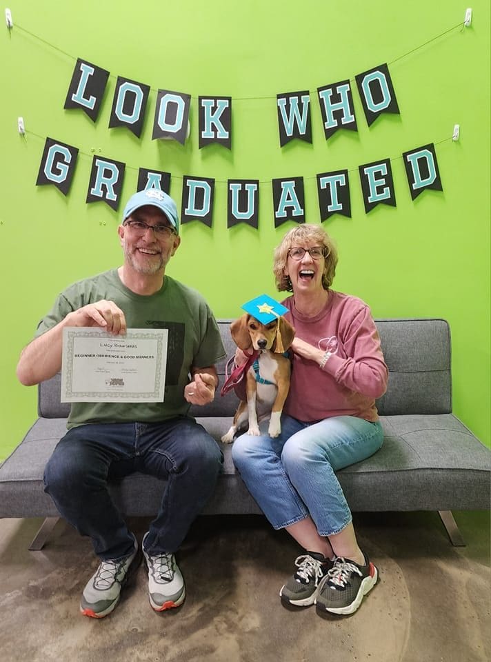 A man and woman sitting on a couch with their dog.