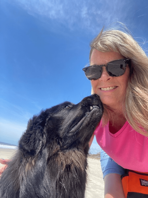 A woman and her dog are kissing on the beach.