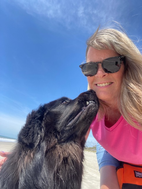 A woman and her dog are kissing on the beach.